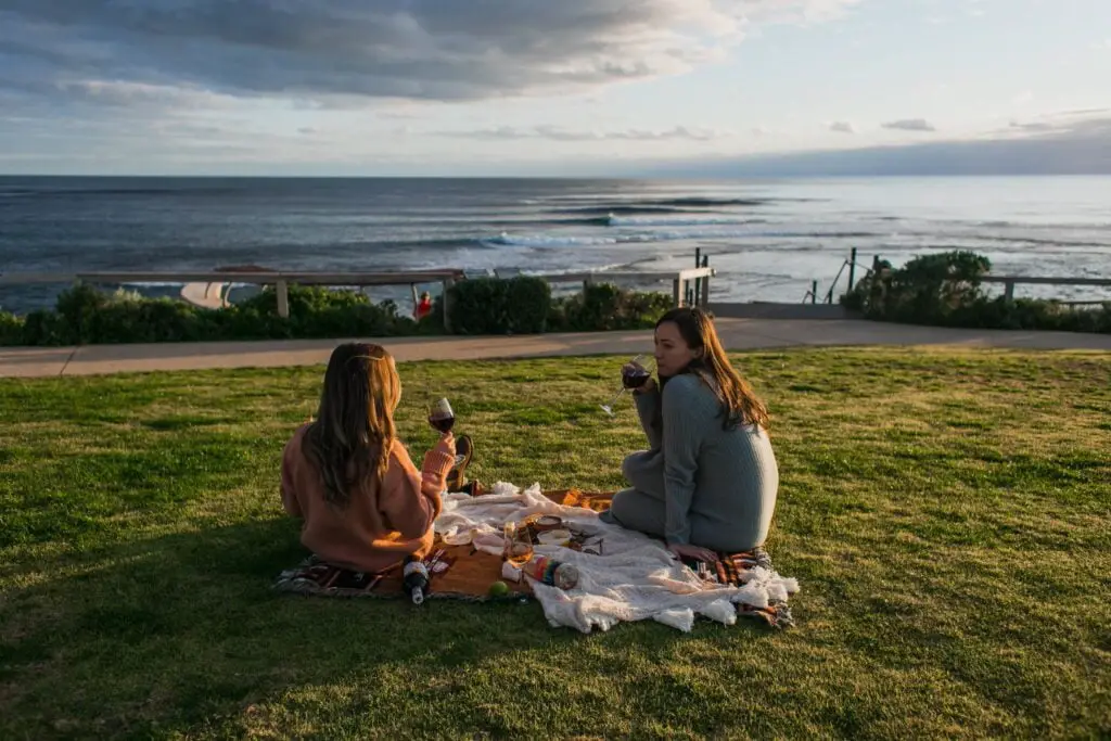 two women are sitting on the grass on the blanket having picninc and talking